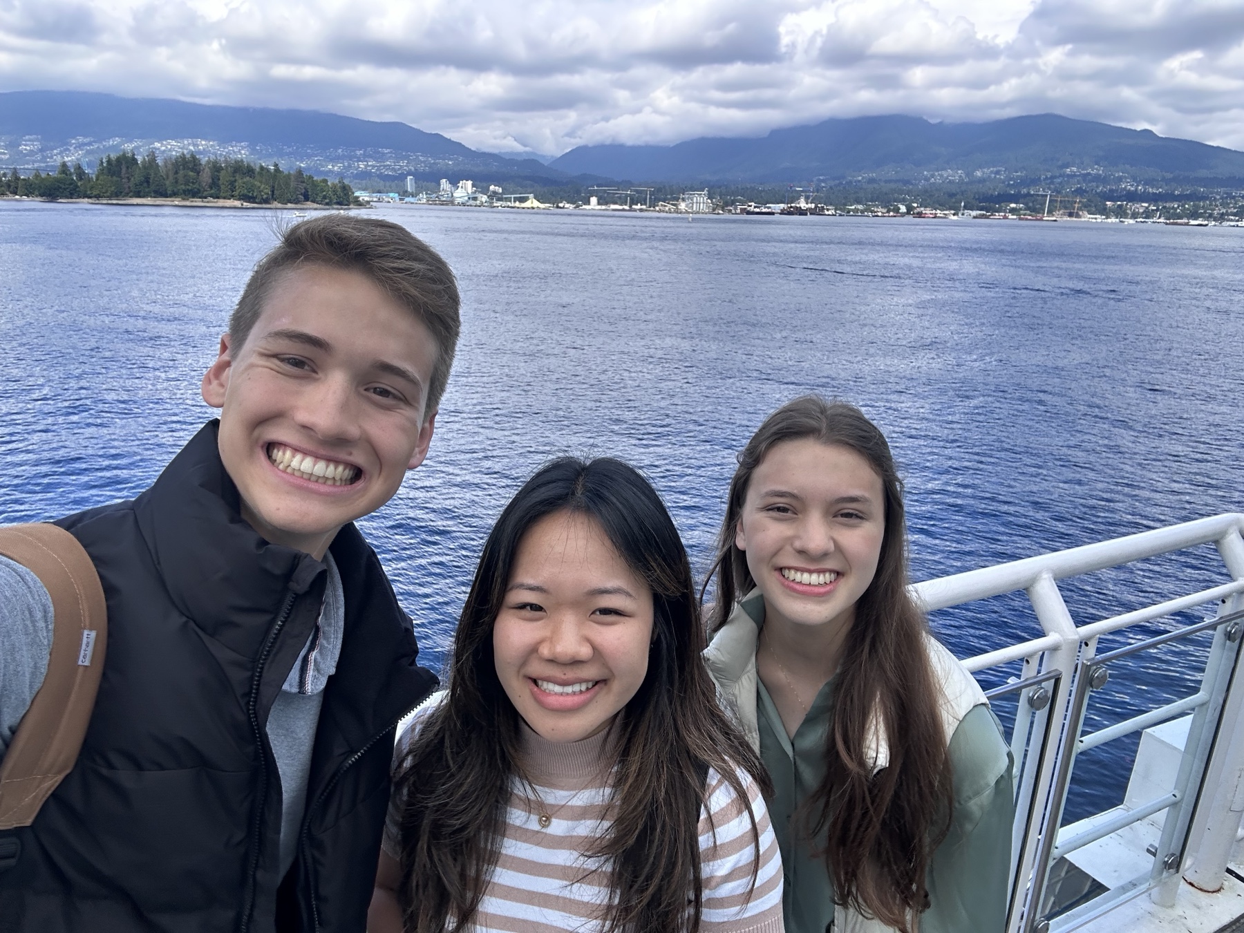 Three friends taking a ferry selfie with mountains across the water