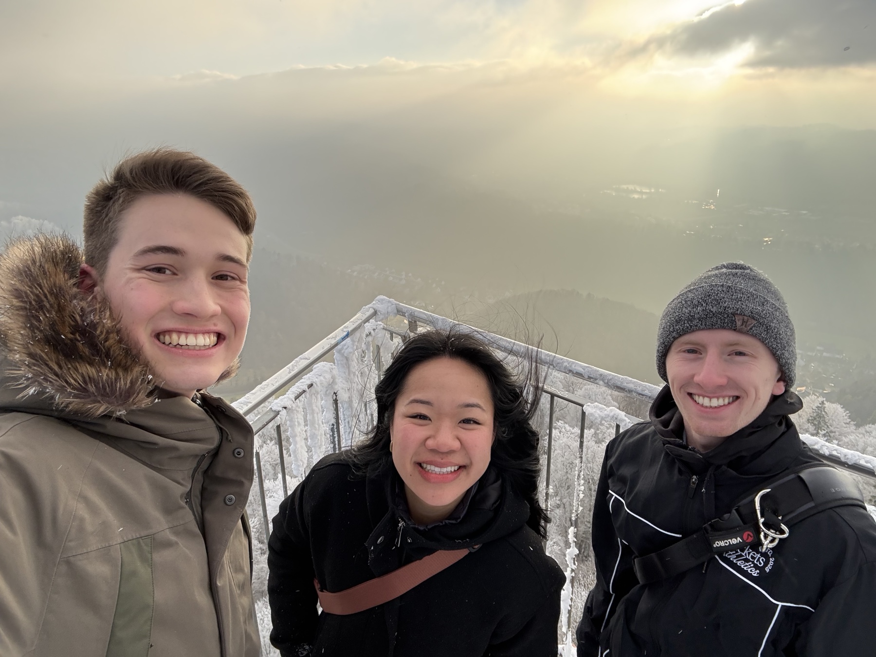 Three friends smiling at a snowy mountain overlook at sunset